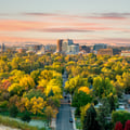 The image shows an aerial view of Boise, Idaho, highlighting its downtown skyline framed by vibrant autumn foliage in the surrounding neighborhoods.