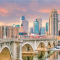 The image appears to show the Minneapolis skyline and the historic Stone Arch Bridge over the Mississippi River in Minnesota.