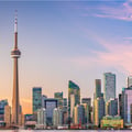 The image shows the CN Tower standing tall beside the bright Toronto skyline at sunset.