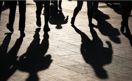 This image shows long, dark shadows of pedestrians walking on a sunlit stone pavement.
