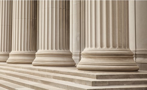 The image shows classic stone columns and steps, which often represent government buildings, courthouses, or legal institutions.