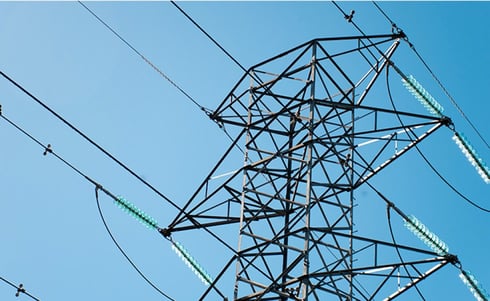 The image appears to show a high-voltage electrical transmission tower, commonly called a pylon or electricity tower, carrying overhead power lines against a clear blue sky.