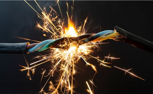 The image shows a dangerous electrical short circuit with exposed, twisted wires producing bright orange and yellow sparks.