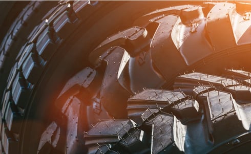 The image shows a close-up of heavy-duty tractor or industrial vehicle tires with deep treads and rubber venting spikes.