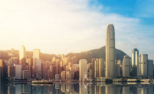 The image shows the iconic skyline of Victoria Harbour in Hong Kong during golden hour, reflecting brilliantly on the calm water's surface.