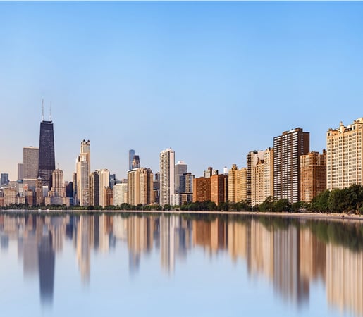 The image shows the Chicago skyline with the John Hancock Center visible on the left, reflected in the calm waters of Lake Michigan along the lakefront.