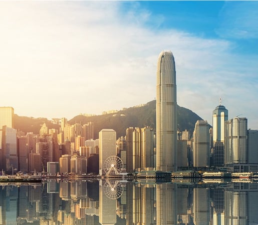 The image shows the iconic skyline of Victoria Harbour in Hong Kong during golden hour, reflecting brilliantly on the calm water's surface.