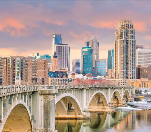 The image appears to show the Minneapolis skyline and the historic Stone Arch Bridge over the Mississippi River in Minnesota.